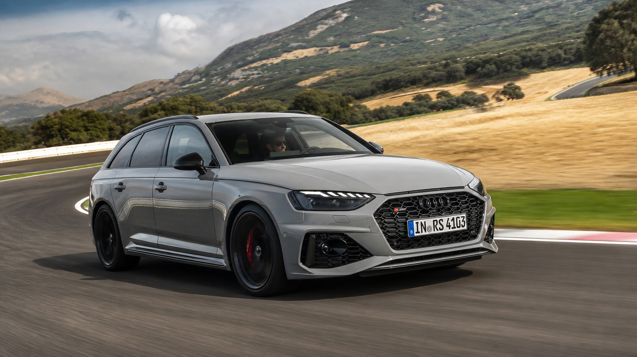 Carro desportivo Audi RS4 Avant cinza a acelerar numa estrada sinuosa com montanhas ao fundo.