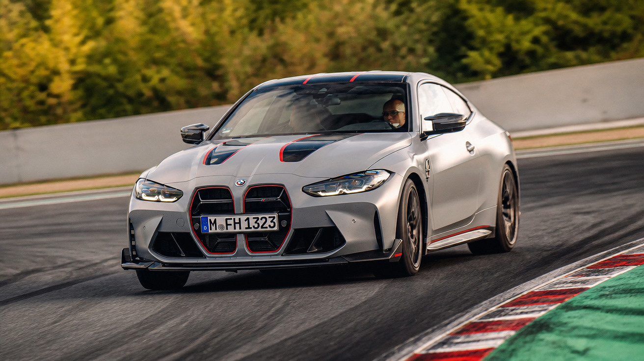 Carro desportivo cinzento BMW a contornar curva em pista de corrida com autódromo ao fundo.