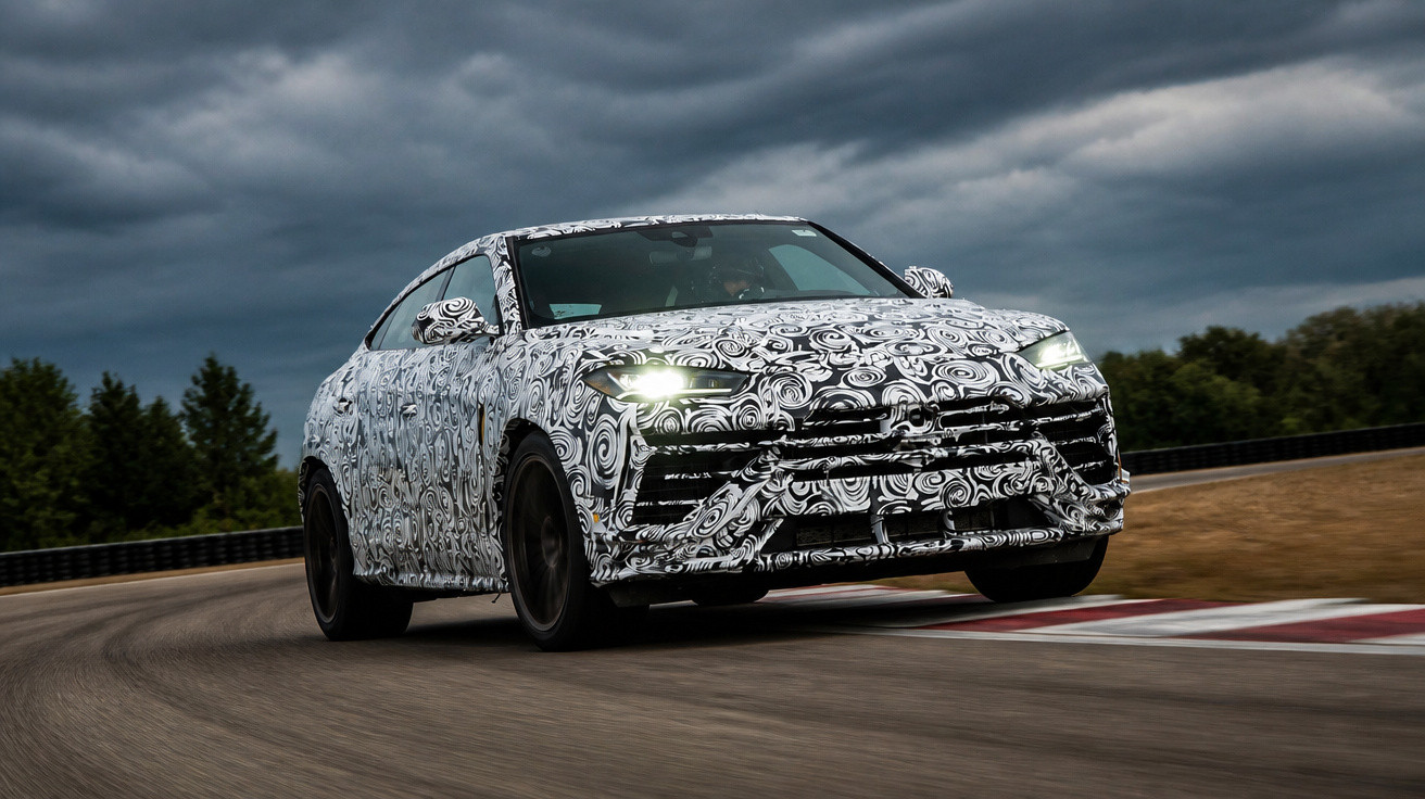 Carro desportivo camuflado em teste, a contornar curva em pista sob céu nublado.