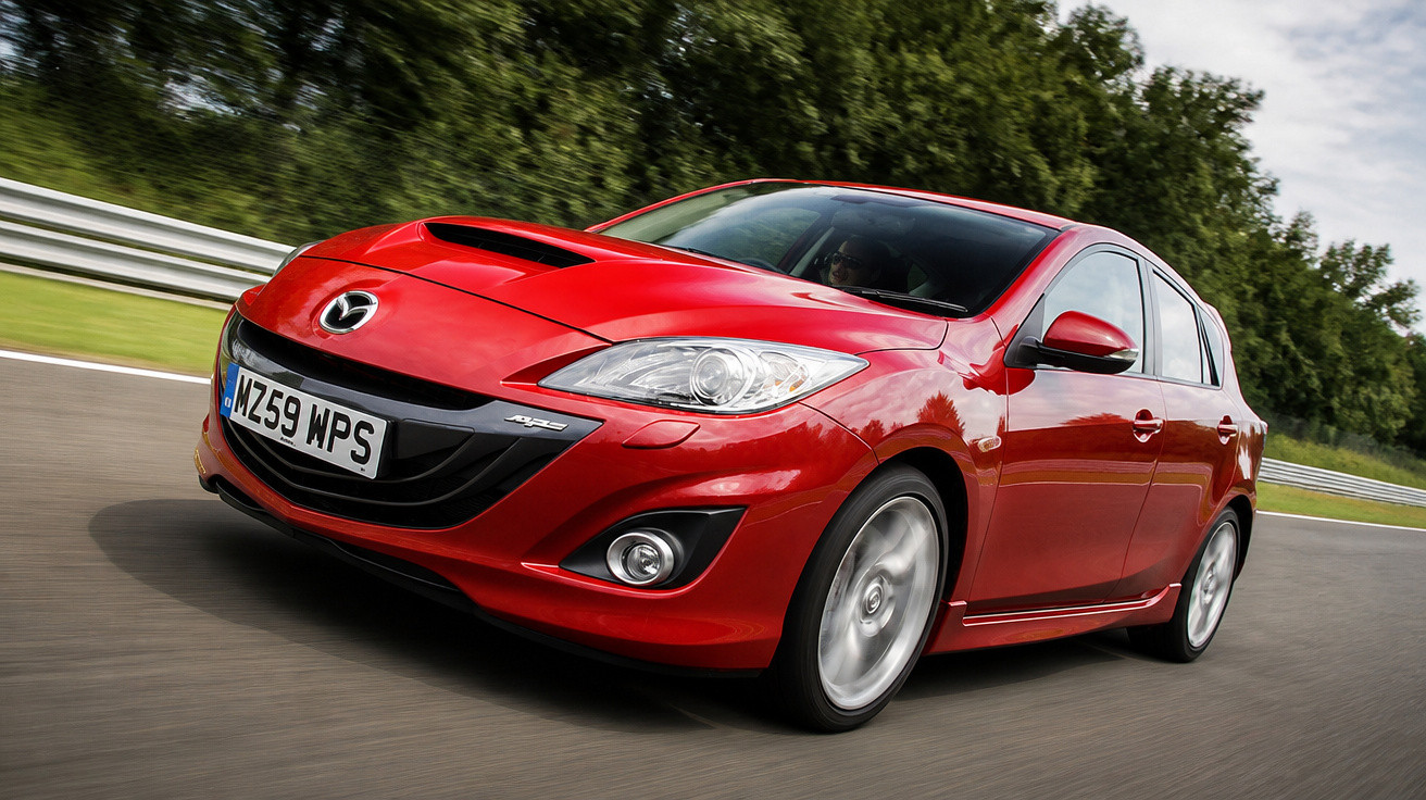 Carro desportivo Mazda vermelho em movimento numa pista com relva e árvores ao fundo.