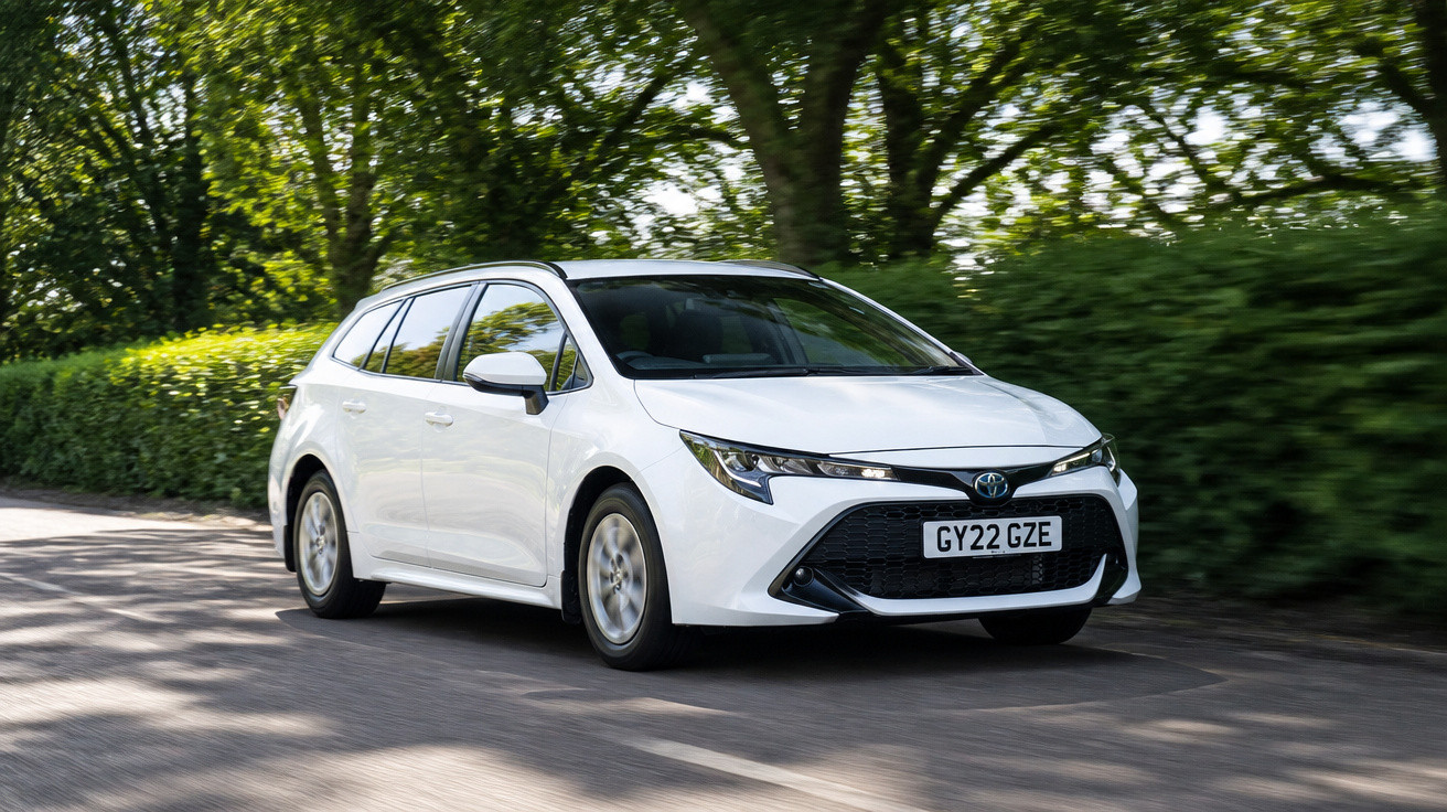 Carro branco Toyota a circular numa estrada ladeada por árvores e vegetação verde.