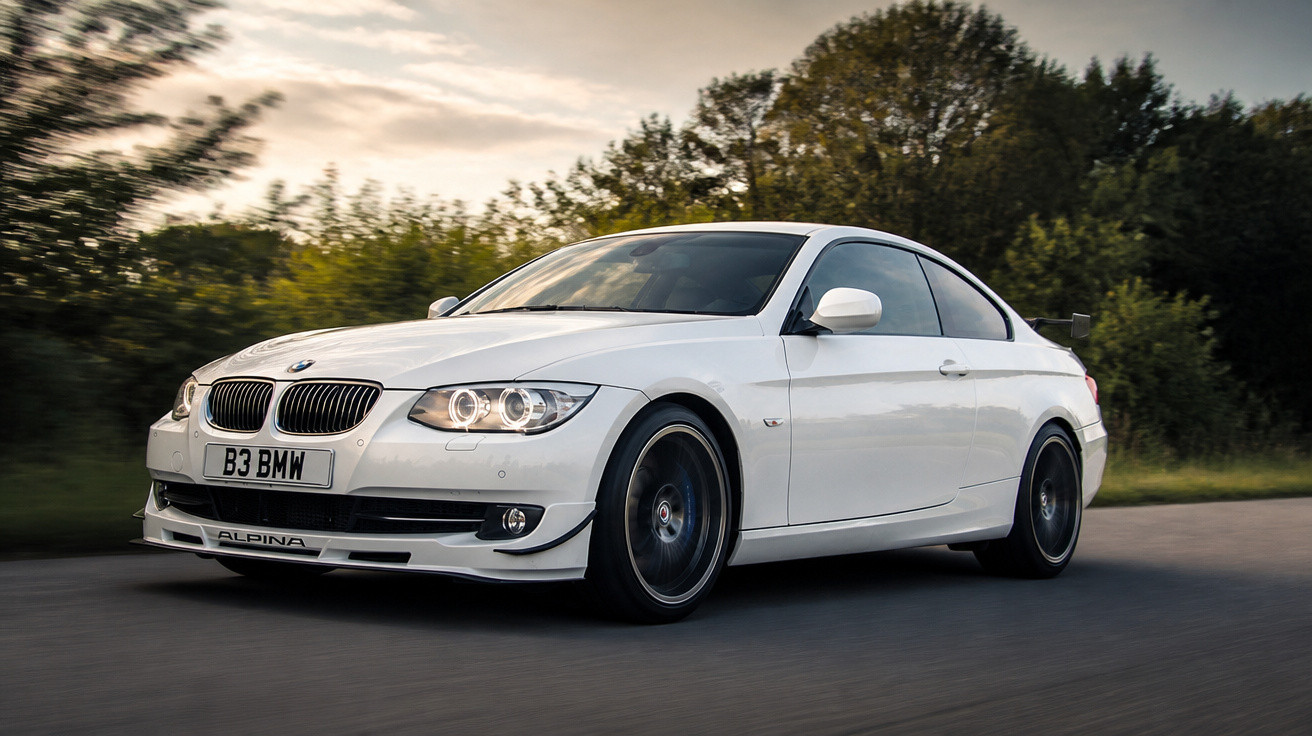 Carro BMW branco a circular numa estrada com árvores ao fundo ao pôr do sol.