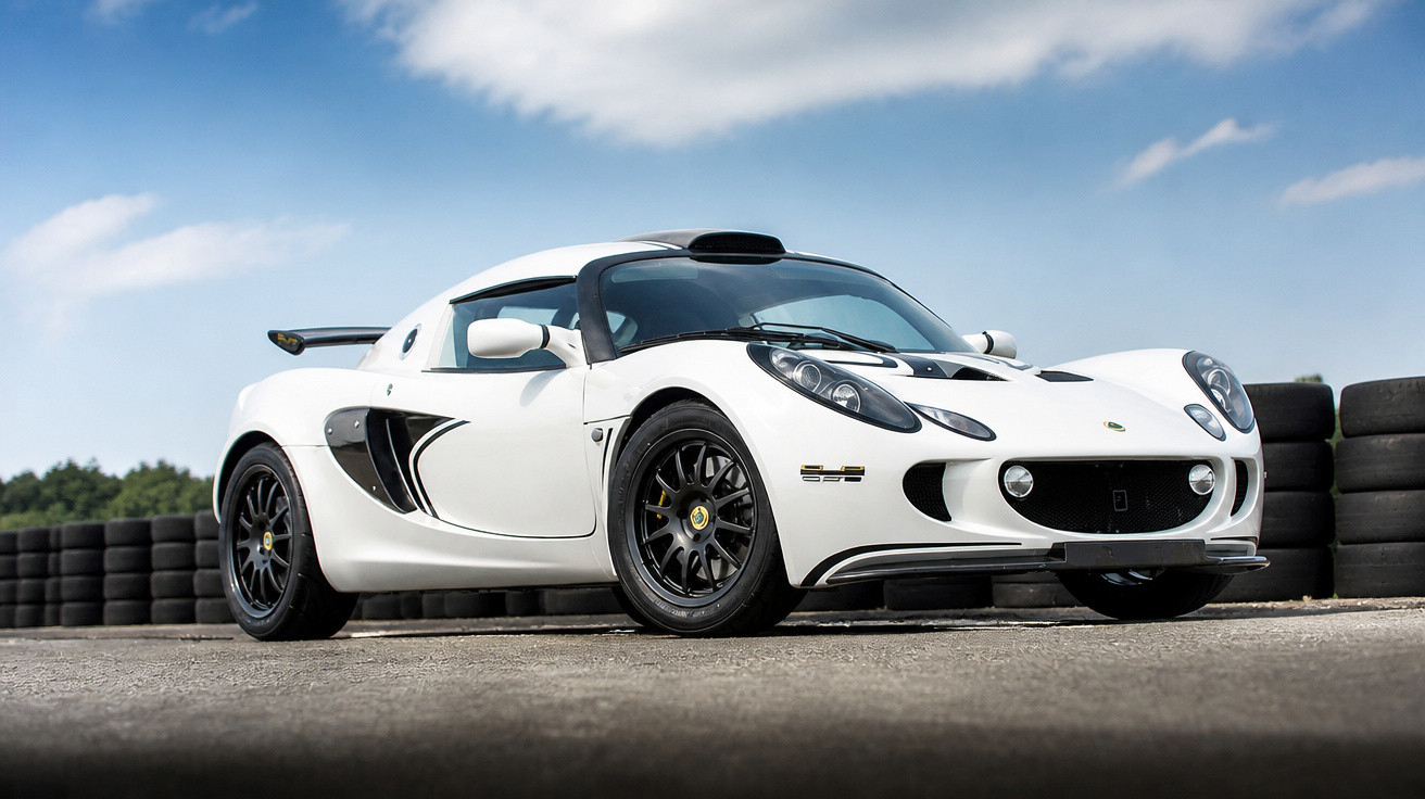 Carro desportivo branco Lotus em pista de corrida com pneus pretos ao fundo e céu azul parcialmente nublado.