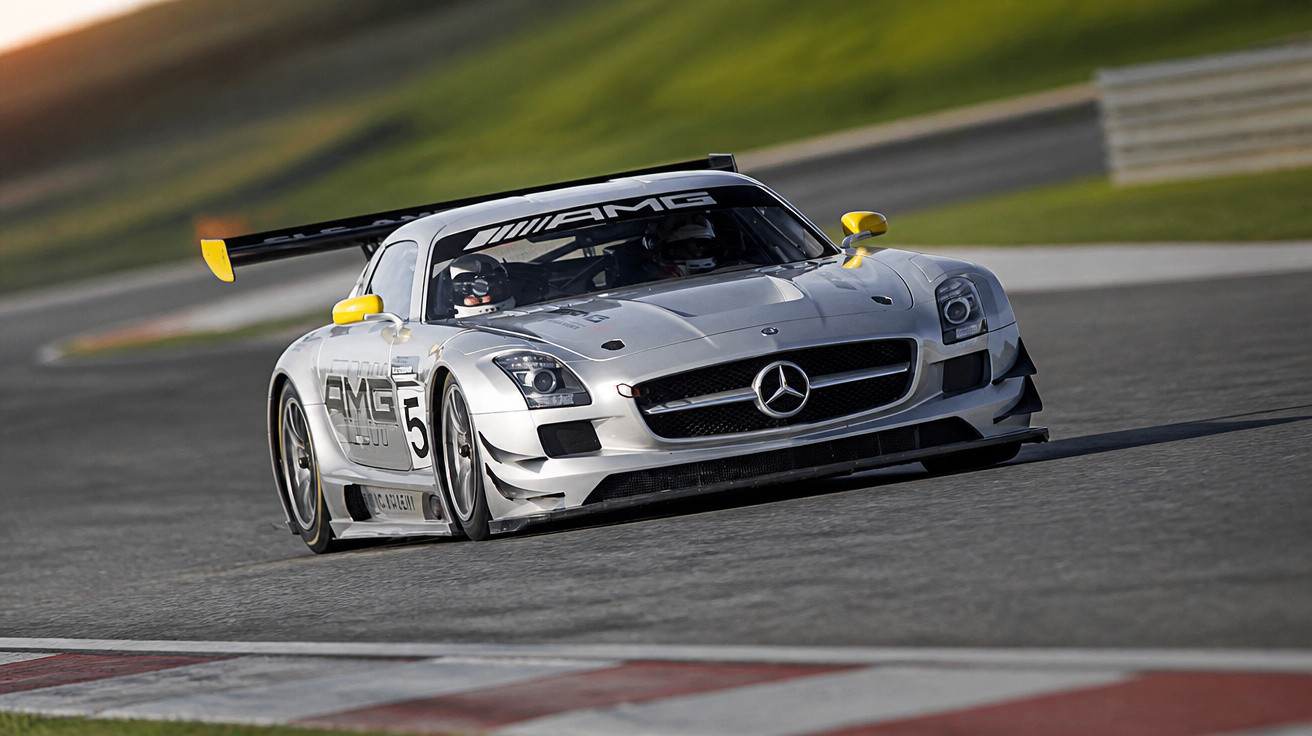 Carro de corrida Mercedes AMG prata a alta velocidade numa pista de circuito com pilotos no interior.