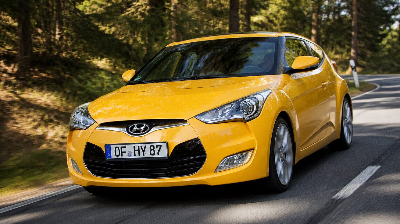 Carro amarelo Hyundai em estrada sinuosa rodeada por árvores numa área florestal.