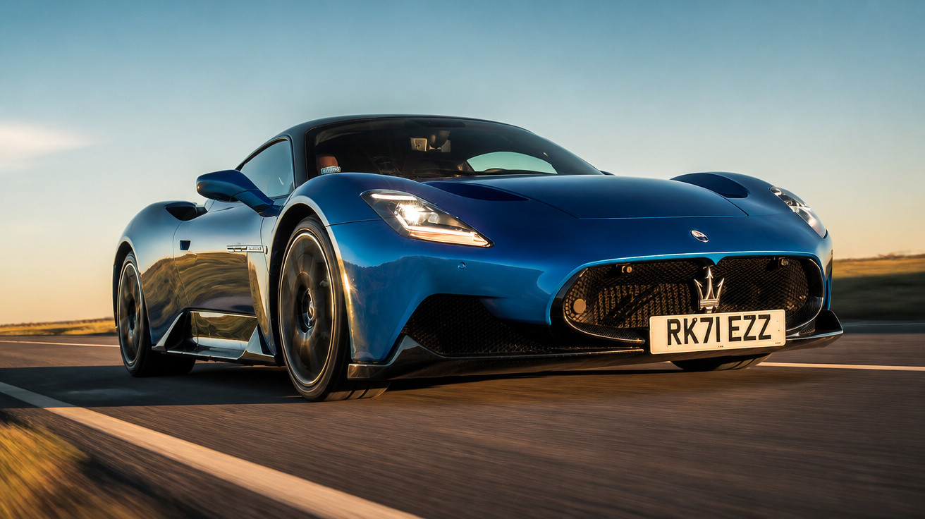 Carro desportivo azul Maserati em estrada ao pôr do sol visto de frente em ângulo baixo.