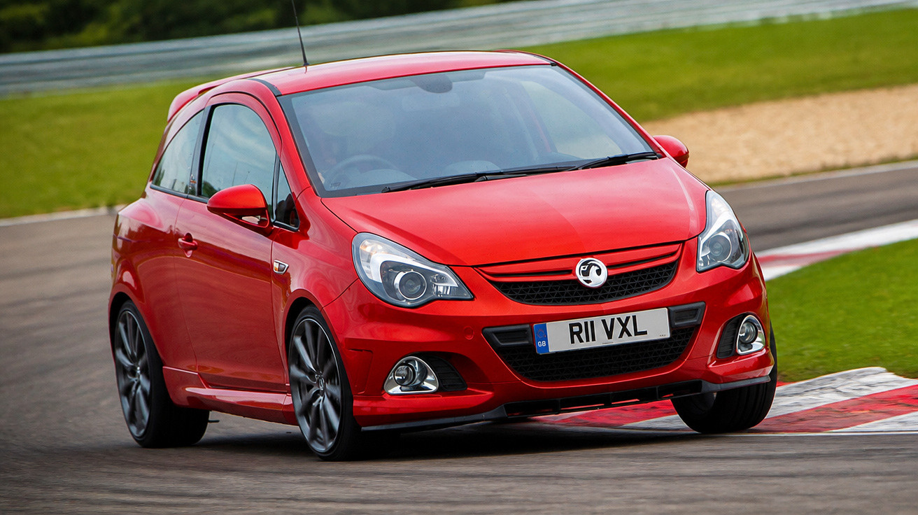 Carro desportivo vermelho a fazer curva numa pista de corrida com piso asfaltado e relva ao redor.