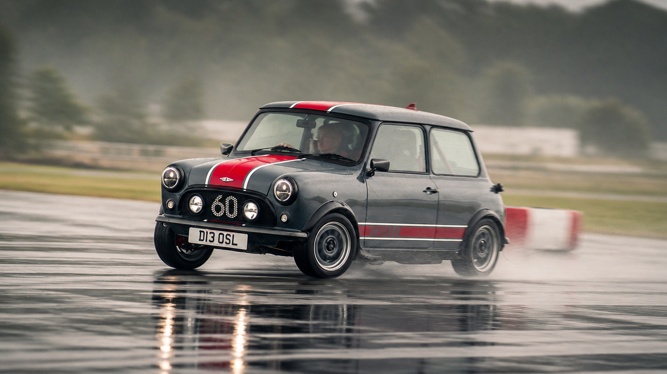 Carro clássico Mini Cooper cinzento com faixa vermelha a fazer derrapagem em pista molhada.