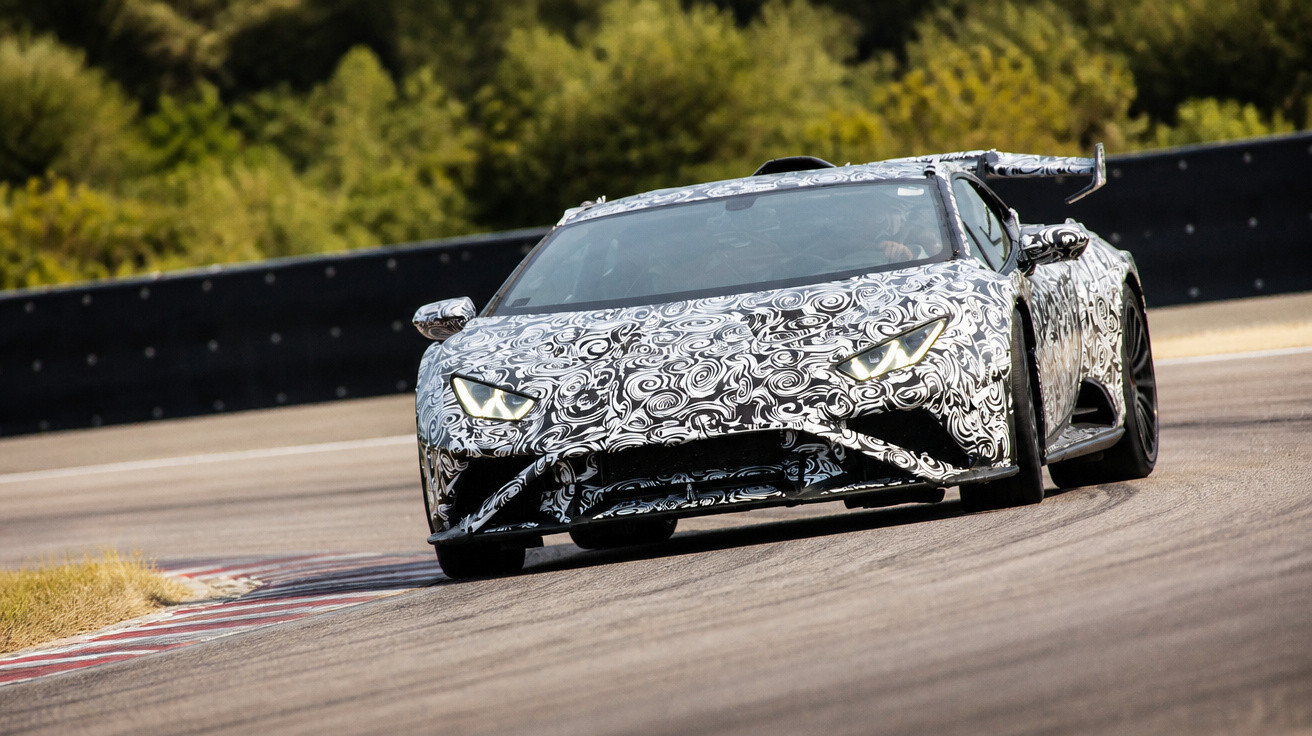 Carro desportivo em testes com camuflagem preta e branca numa curva de pista de corrida ao ar livre.