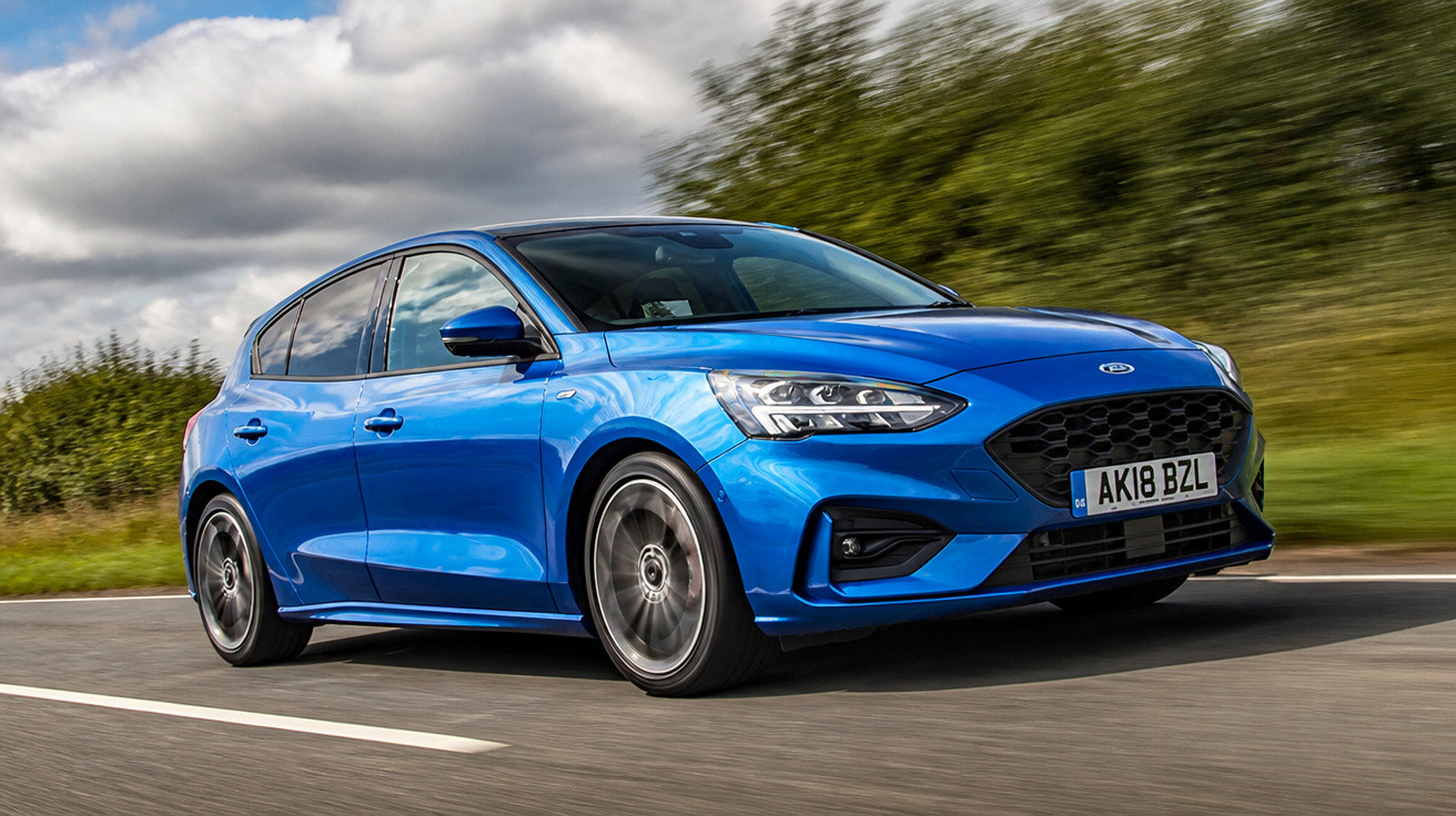 Carro azul desportivo Ford Focus a circular numa estrada com vegetação ao fundo e céu nublado.