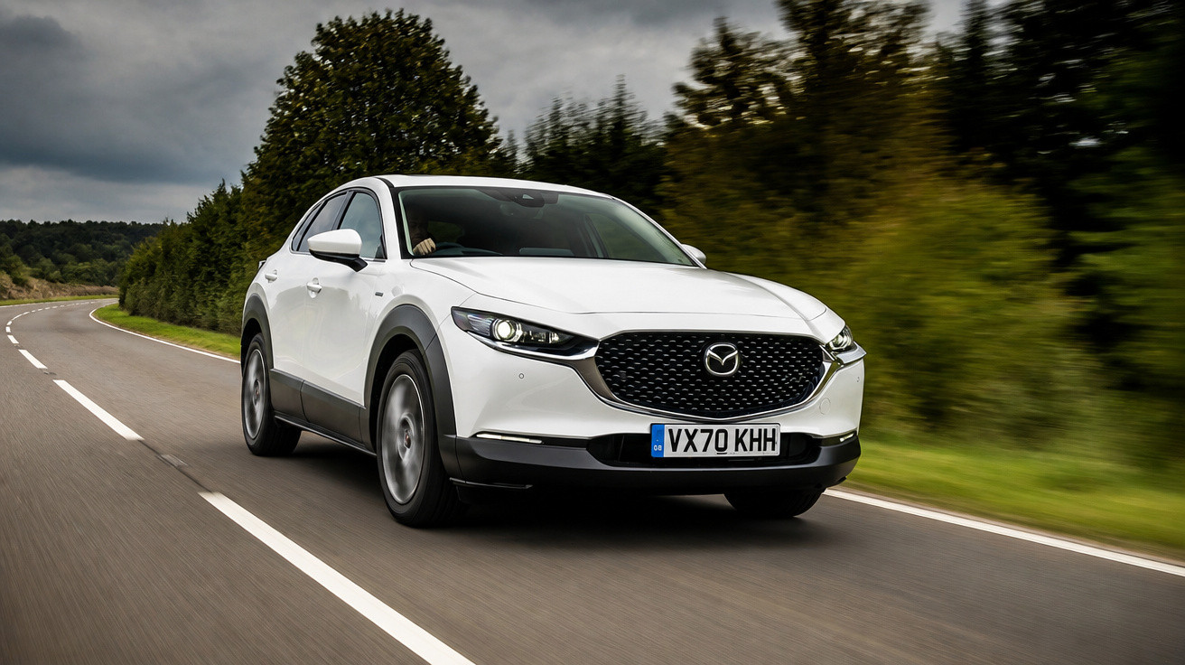 Carro branco Mazda a circular numa estrada sinuosa rodeada por árvores sob céu nublado.