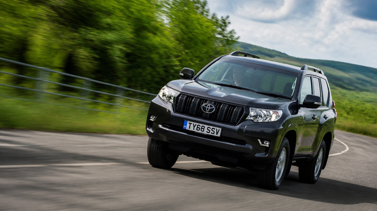 Carro preto SUV Toyota em curva numa estrada rodeada de vegetação verde e colinas ao fundo.