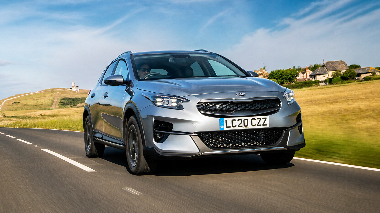 Automóvel cinzento Kia a circular numa estrada rural com céu azul e campo ao redor.