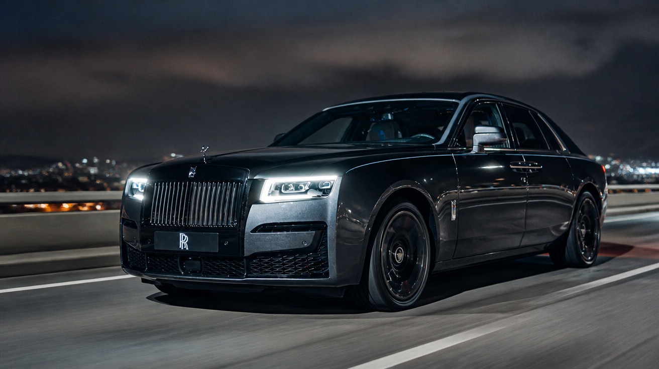 Carro de luxo Rolls-Royce cinza escuro a circular numa estrada urbana à noite.