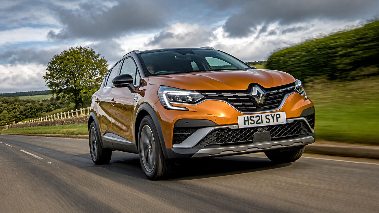 Carro Renault laranja a circular numa estrada rodeada de campo e árvores sob céu nublado.