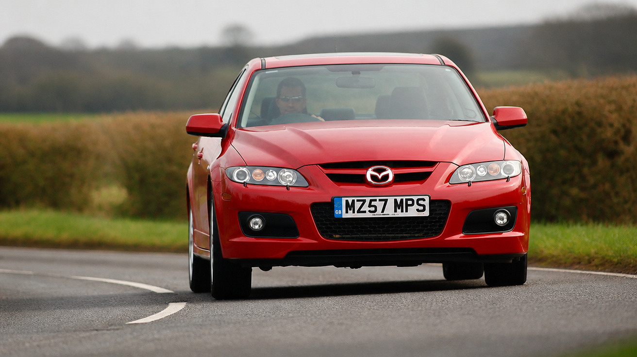 Carro desportivo vermelho Mazda a circular numa estrada sinuosa com vegetação ao fundo.