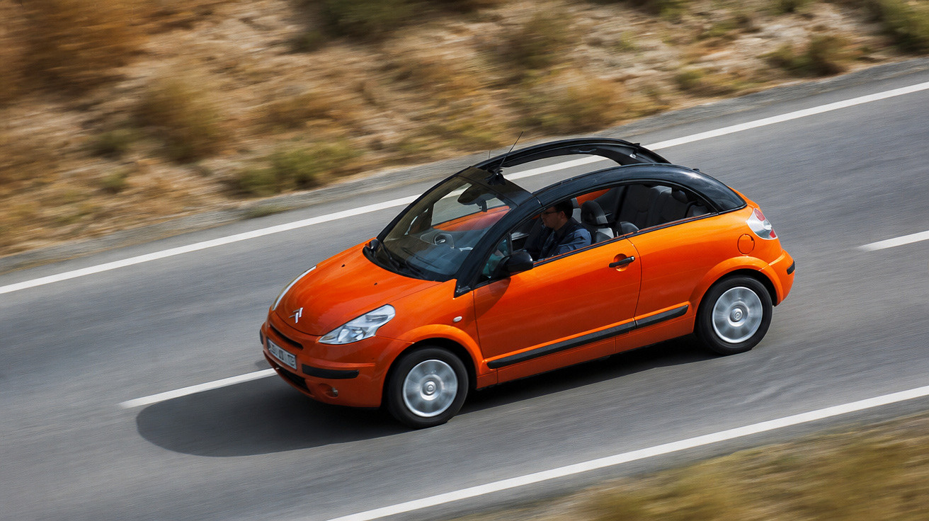 Carro Citroën amarelo a circular numa estrada asfaltada com paisagem seca em redor.