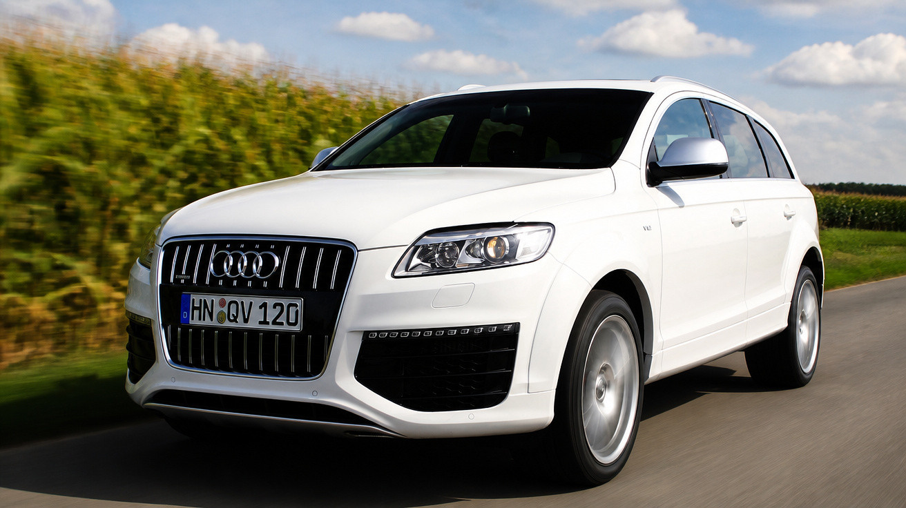Carro Audi SUV branco a circular numa estrada rural com céu azul e campos verdes ao fundo.