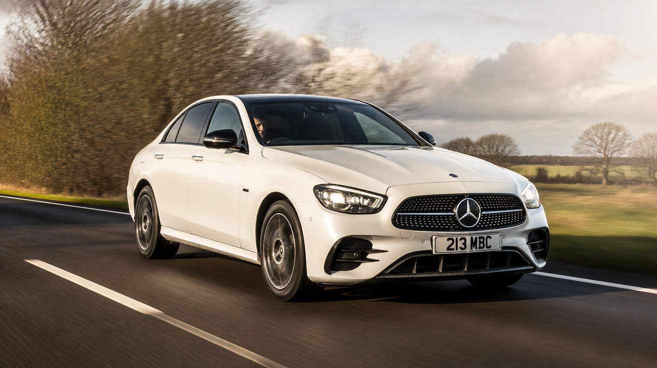 Carro branco Mercedes-Benz a circular numa estrada em área rural com árvores e céu nublado ao fundo.