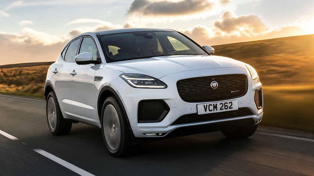 Automóvel SUV branco Jaguar a circular numa estrada ao pôr do sol com céu parcialmente nublado.