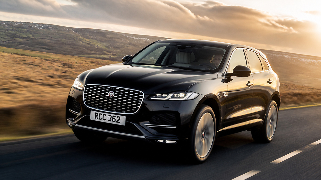 Carro preto Jaguar SUV em estrada com paisagem montanhosa ao pôr do sol.