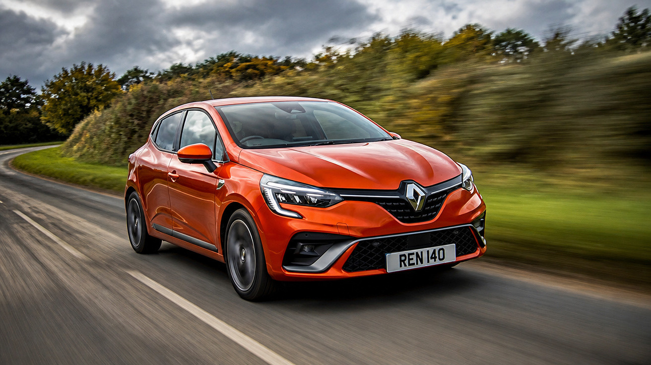 Carro Renault Clio laranja em movimento numa estrada rodeada por árvores com céu nublado.