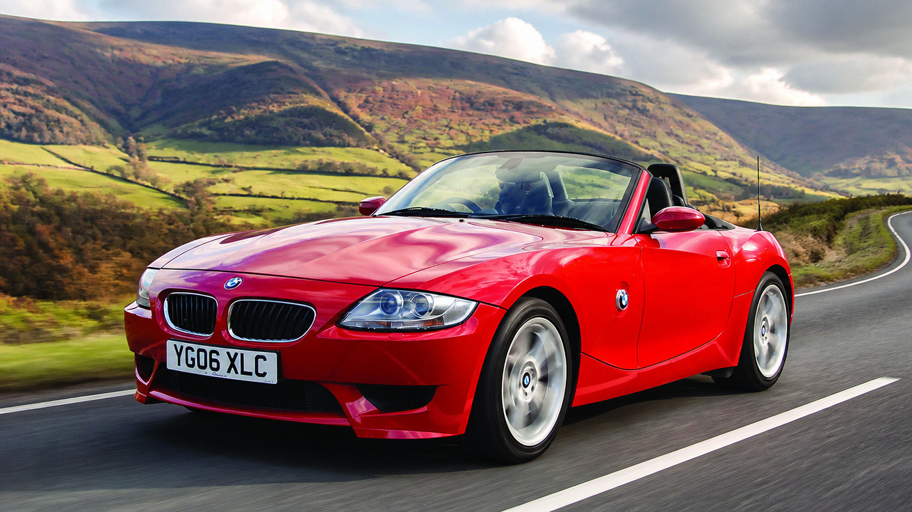 Carro desportivo vermelho BMW descapotável a circular numa estrada com colinas verdes ao fundo.