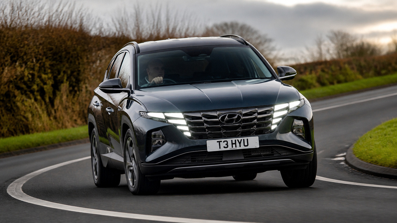 Carro Hyundai SUV preto em curva numa estrada rodeada de relva e árvores secas ao pôr do sol.