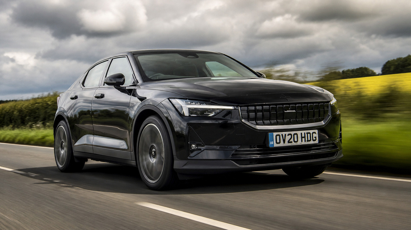 Carro elétrico preto Polestar 2 em movimento numa estrada rodeada de vegetação e campos amarelos.