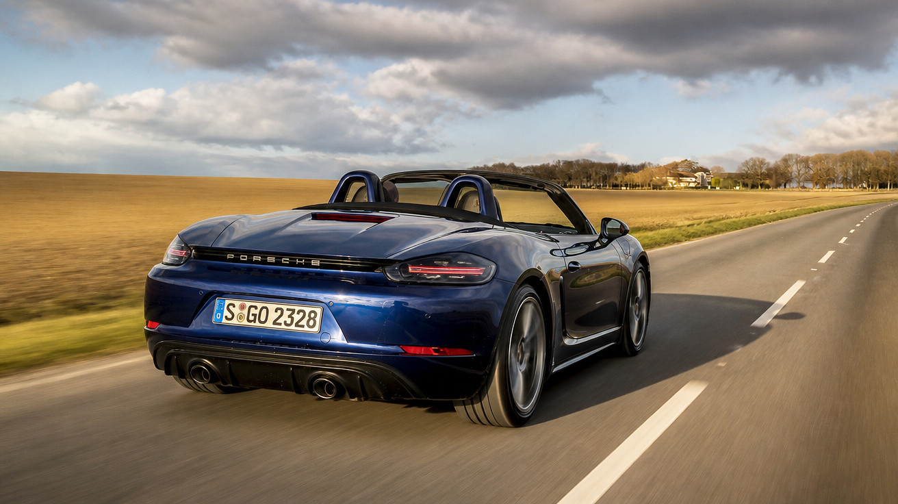 Carro desportivo azul conversível Porsche a conduzir numa estrada rural sob céu nublado.