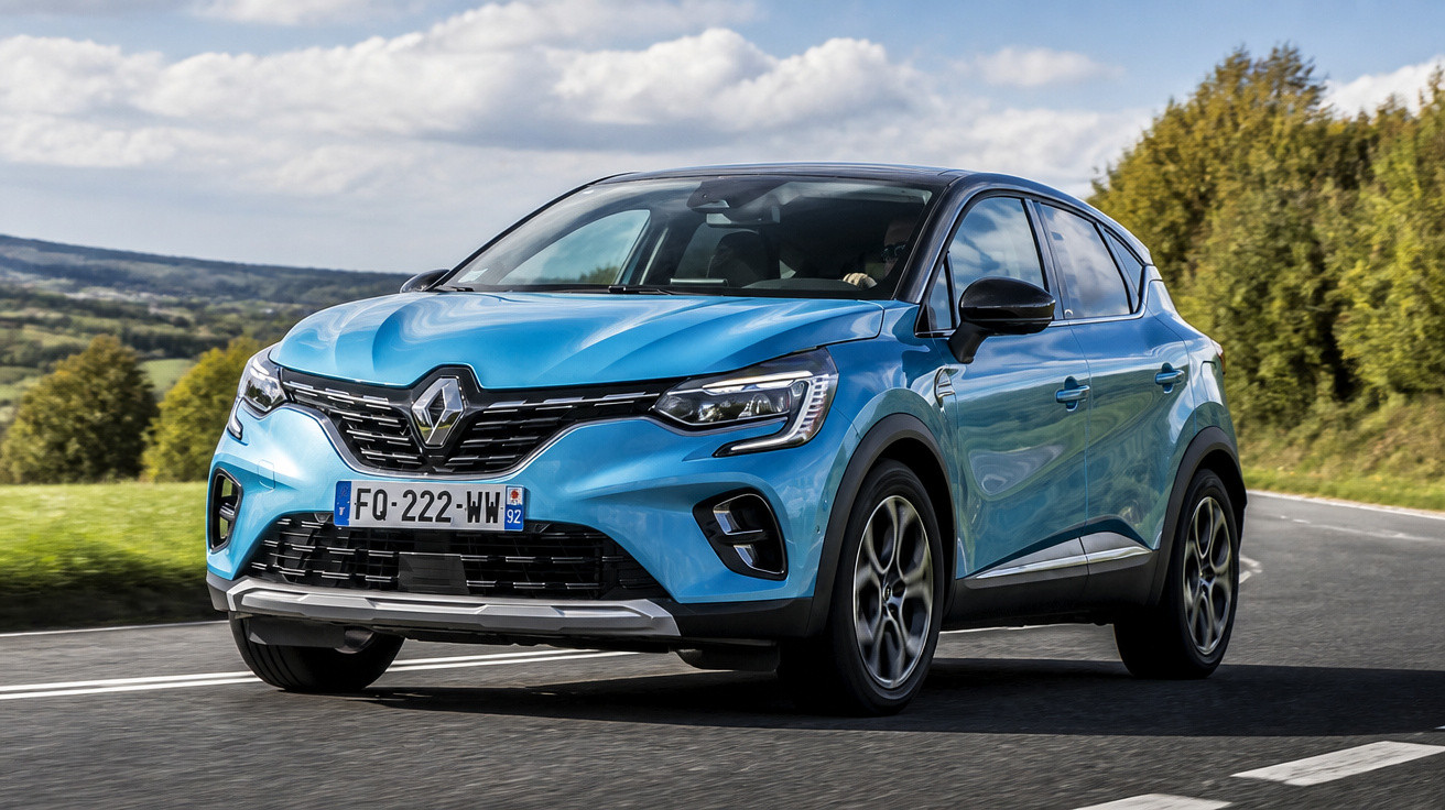 Carro SUV azul Renault circula numa estrada asfaltada com vegetação e céu nublado ao fundo.