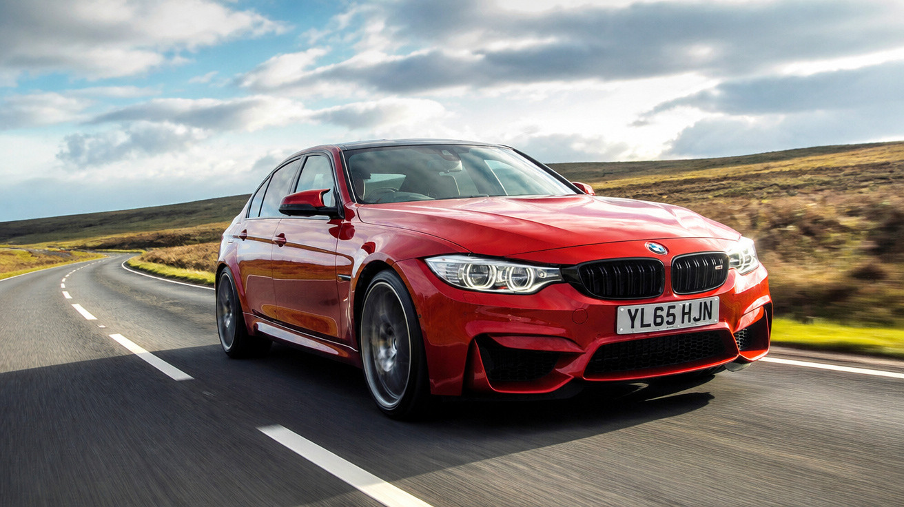 Carro desportivo vermelho BMW circula numa estrada sinuosa em dia com céu parcialmente nublado.