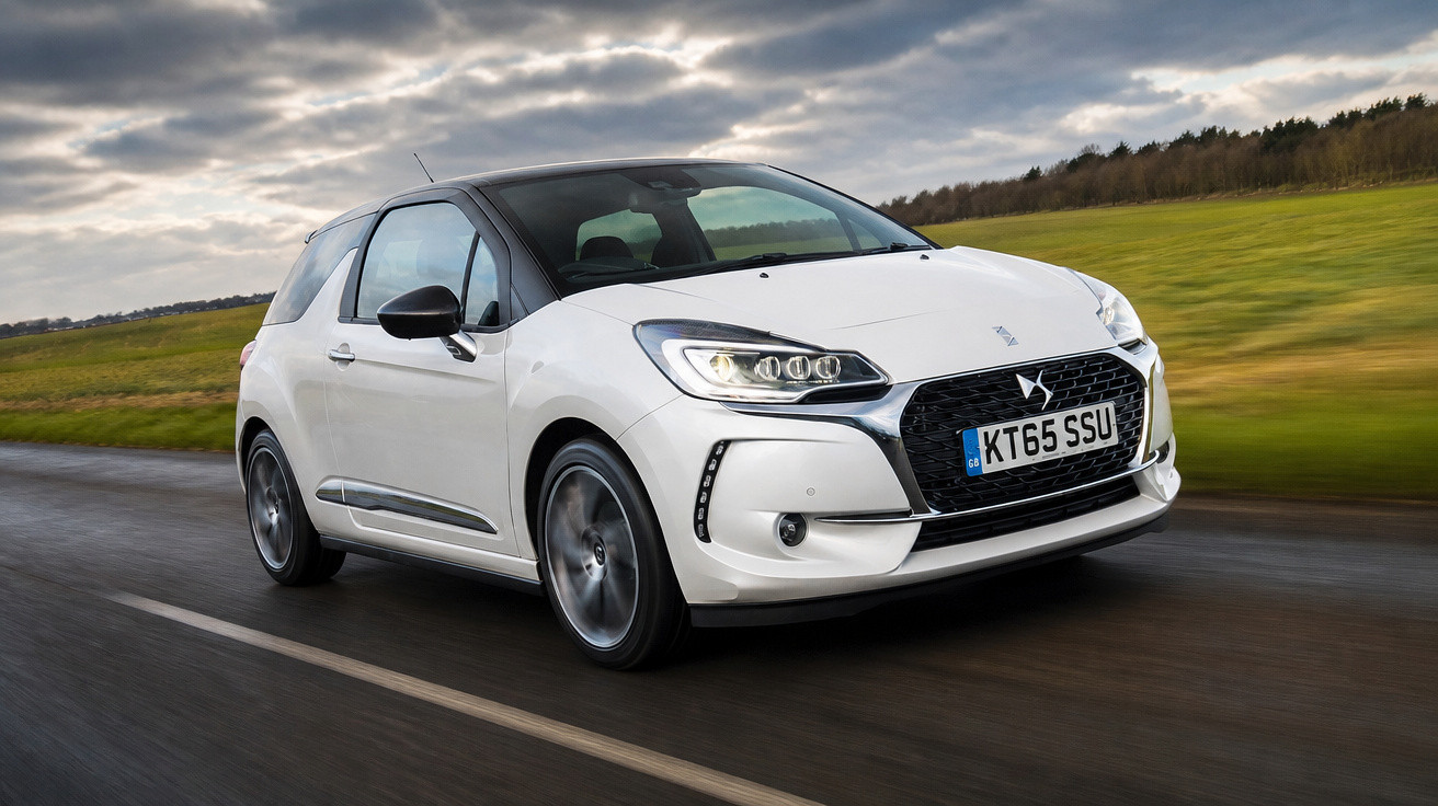 Carro branco DS 3 em movimento numa estrada com céu nublado e campo verde ao fundo.