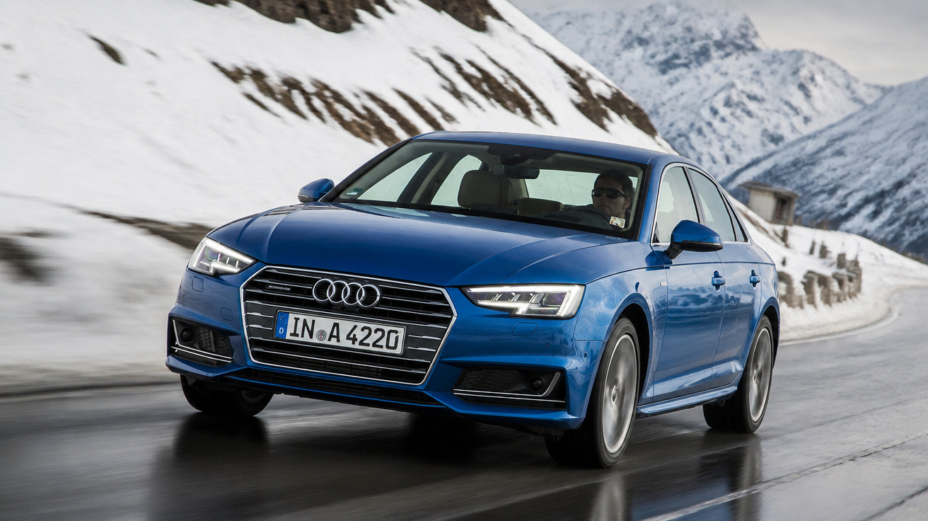 Carro Audi azul a conduzir numa estrada molhada com montanhas e neve ao fundo.