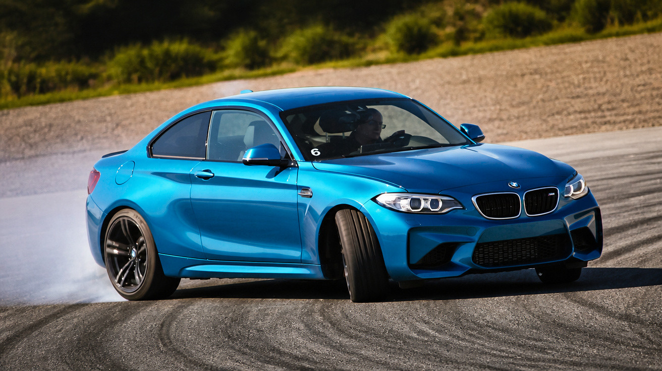 Carro desportivo azul a derrapar numa curva numa pista de corrida ao ar livre.