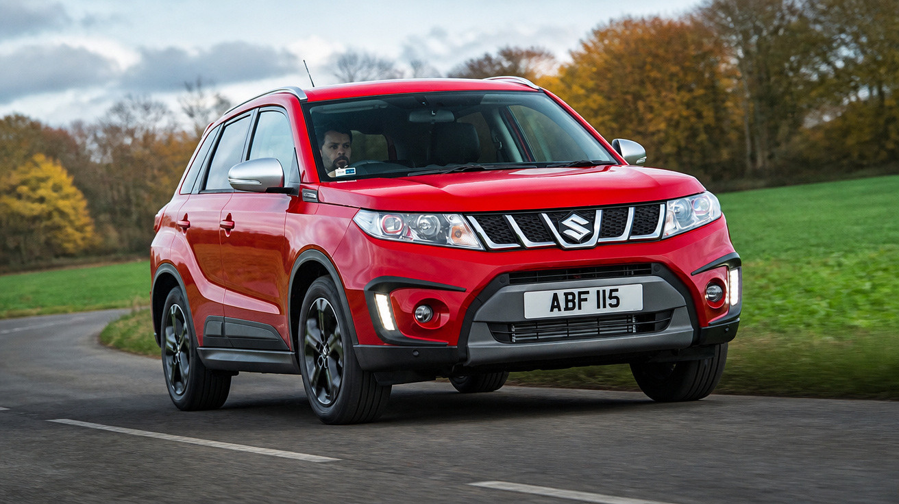Carro SUV vermelho Suzuki a circular numa estrada rural com campos e árvores outonais ao fundo.