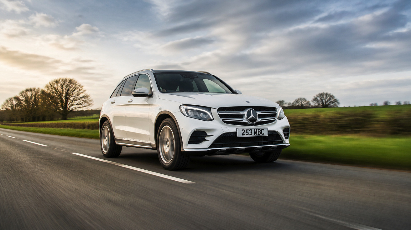 Carro branco Mercedes-Benz a conduzir numa estrada rural com céu nublado e árvores ao fundo.