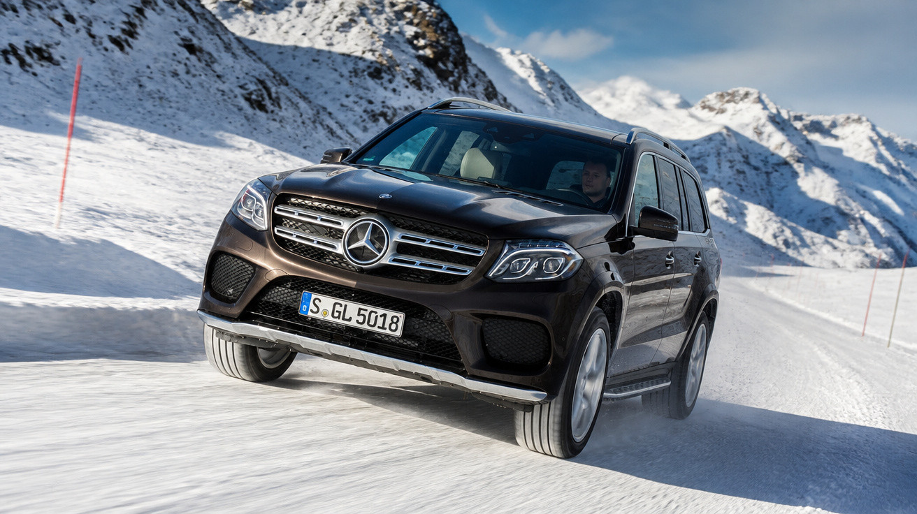 Carro SUV Mercedes-Benz preto a circular em estrada coberta de neve nas montanhas.