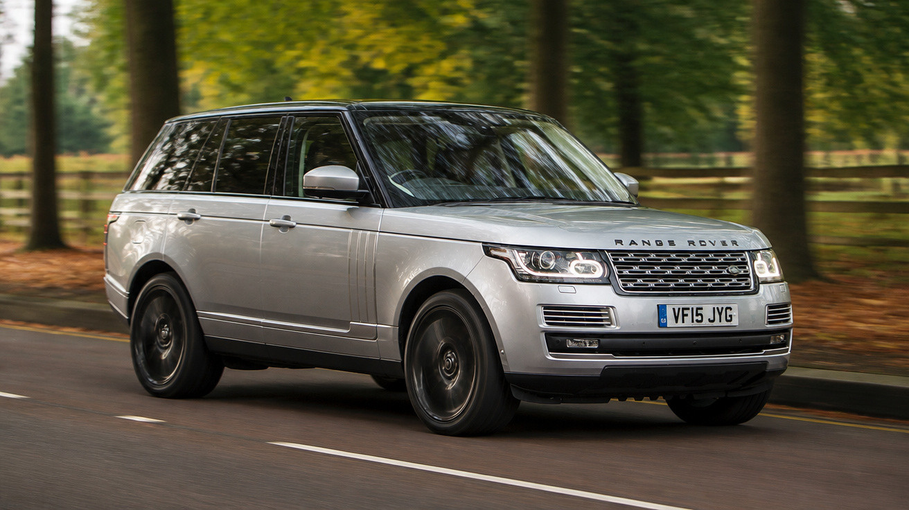 Carro Range Rover cinzento em movimento numa estrada rodeada por árvores verdes.