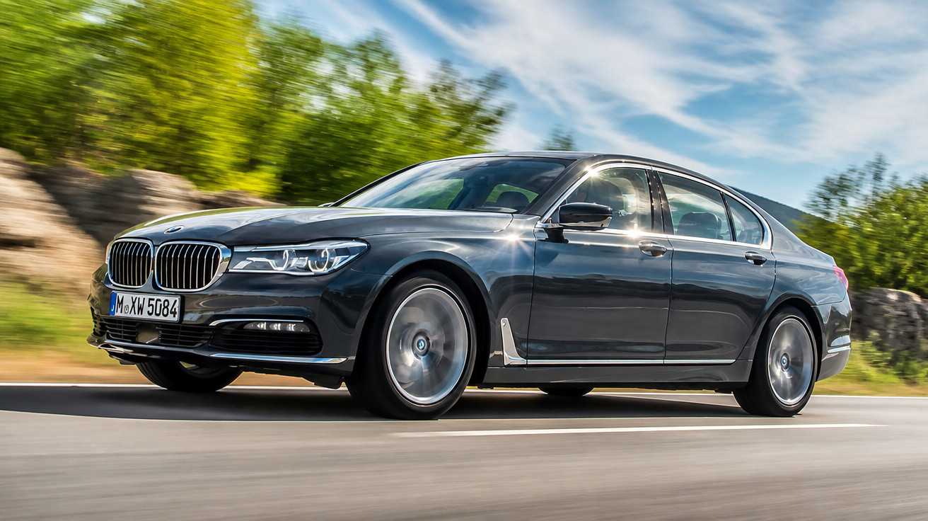 Carro BMW preto em movimento numa estrada rodeada de vegetação verde sob céu azul.