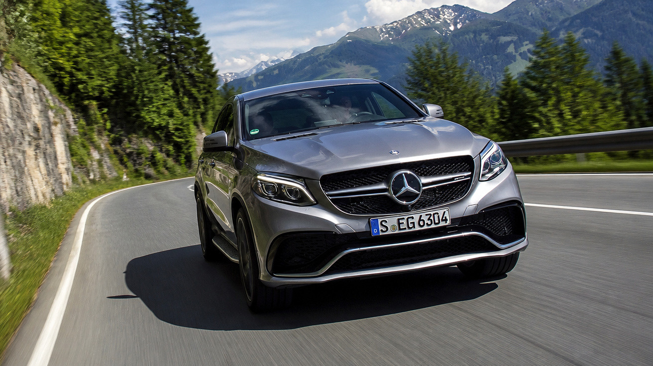 Carro Mercedes-Benz cinzento a conduzir numa estrada sinuosa com montanhas e árvores ao fundo.