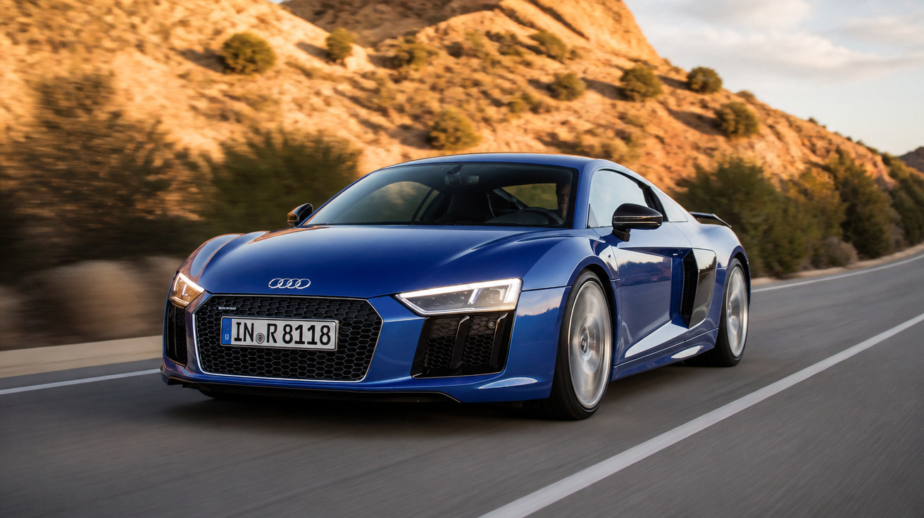 Carro desportivo azul Audi R8 em estrada sinuosa com colinas rochosas ao fundo ao pôr do sol.