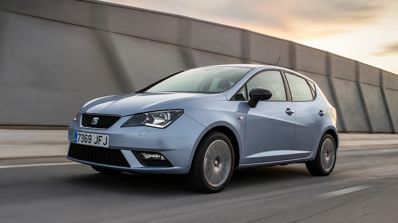 Carro cinzento Seat ibiza a circular numa estrada urbana com muro cinzento ao fundo ao pôr-do-sol.