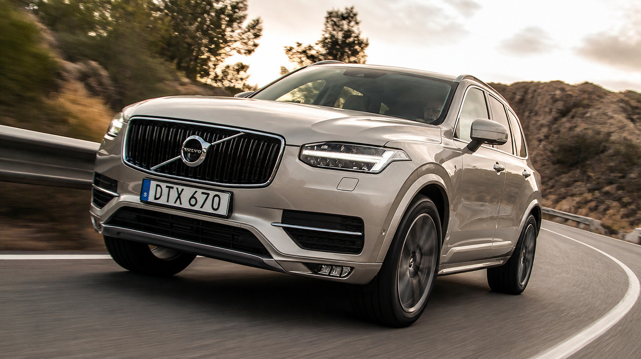 Carro Volvo cinzento a circular numa estrada sinuosa rodeada de paisagem montanhosa.