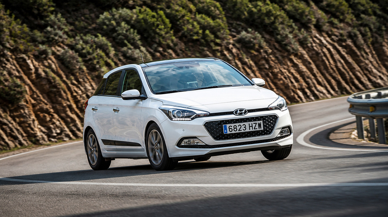 Carro branco Hyundai a circular numa estrada curva com relva e rochas ao fundo.