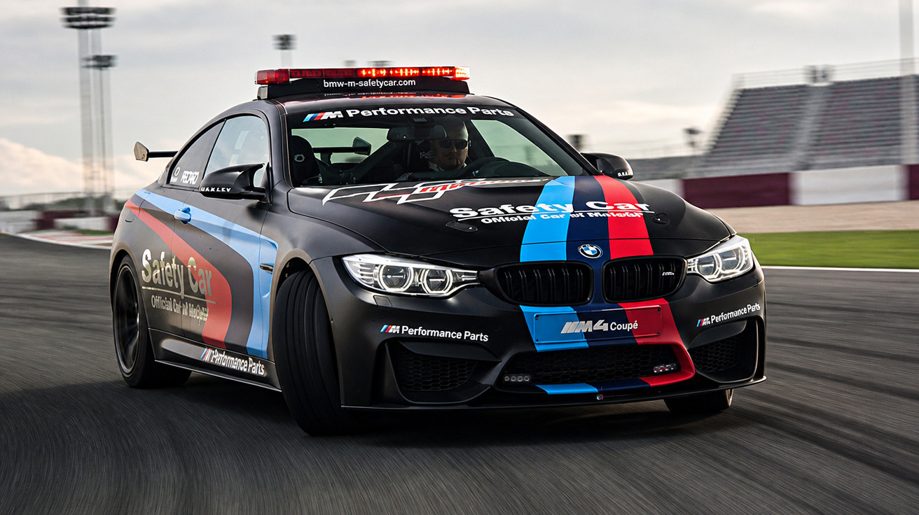 Carro BMW M4 Safety Car Preto com faixas azuis e vermelhas em circuito de corridas.