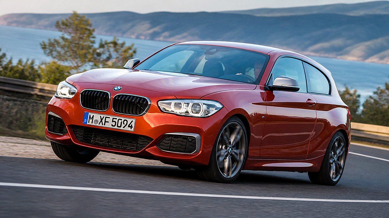 Carro desportivo vermelho BMW a circular numa estrada sinuosa junto ao mar e montanhas ao fundo.