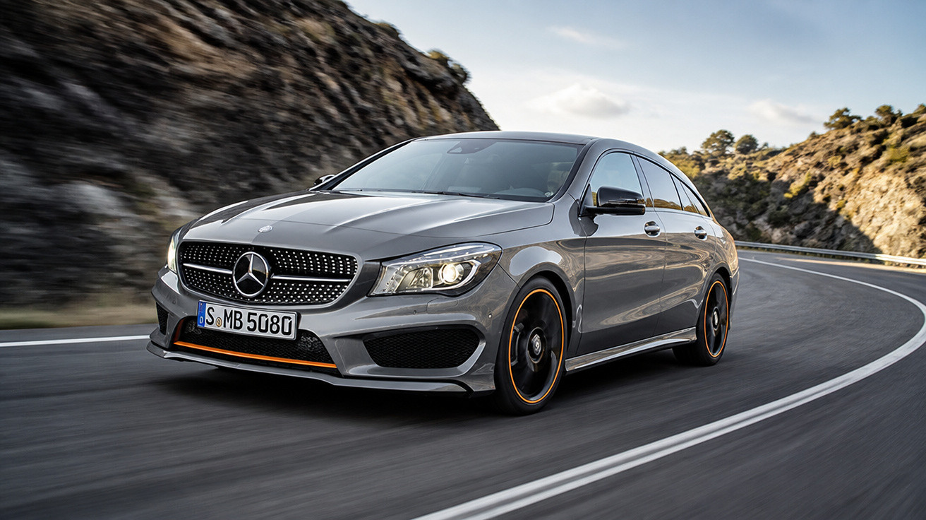 Carro Mercedes-Benz cinzento em curva numa estrada de montanha sob céu nublado.