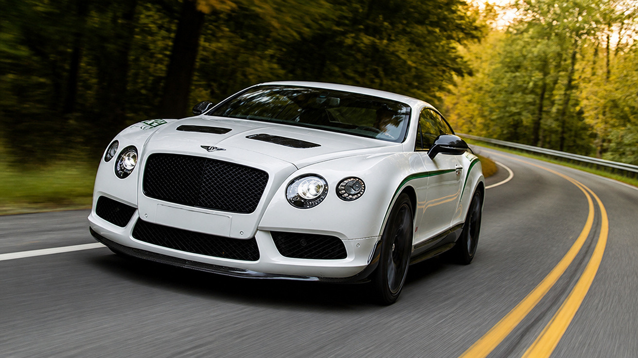 Carro desportivo branco a circular numa estrada sinuosa rodeada de árvores verdes.