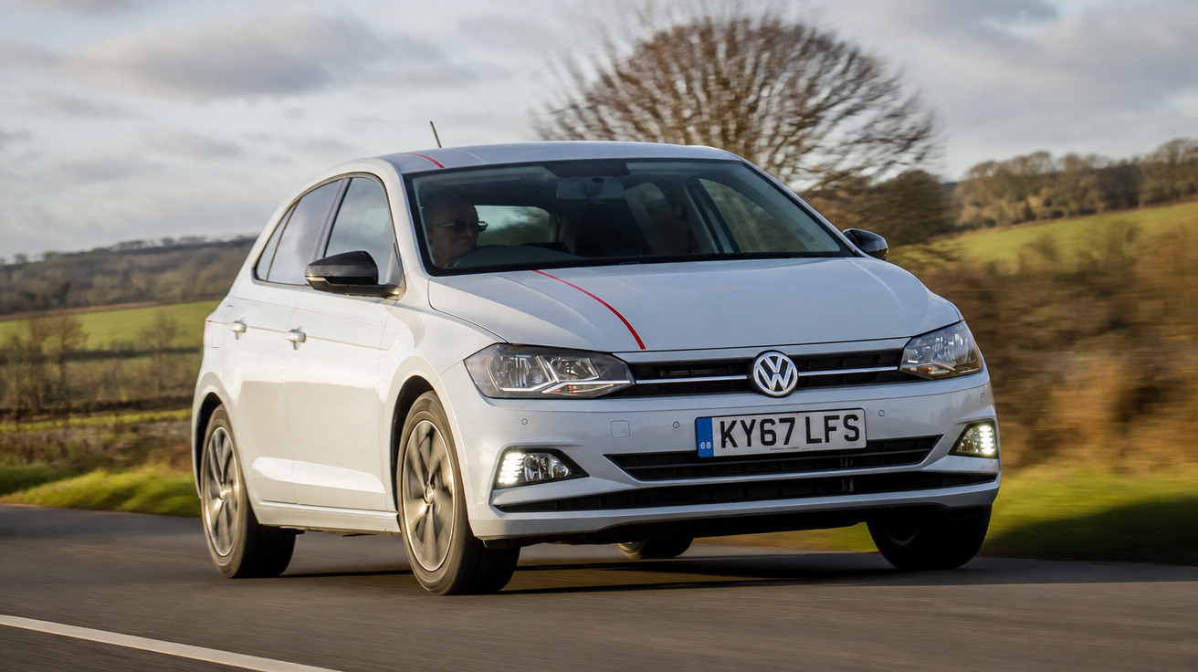 Carro branco Volkswagen em movimento numa estrada rural com paisagem campestre ao fundo.
